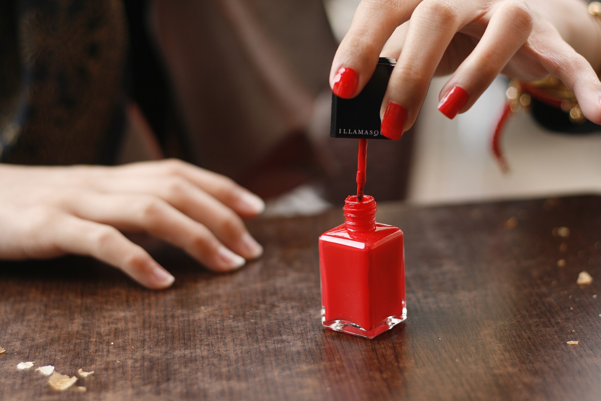 Mano con las uñas pintadas de rojo destapando un esmalte